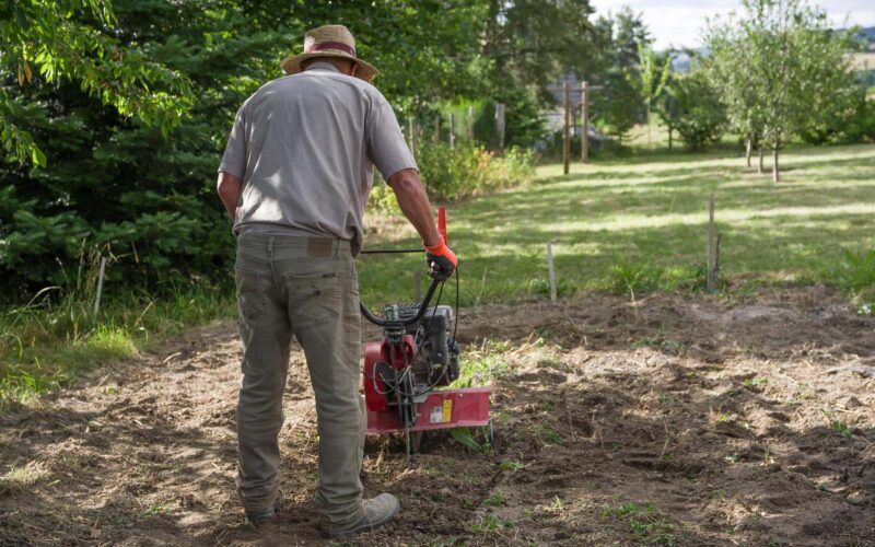 A man operating a rototiller in a garden